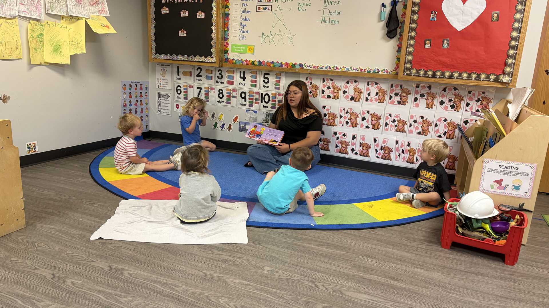 Teacher reading with early preschoolers on a rainbow circle-time rug