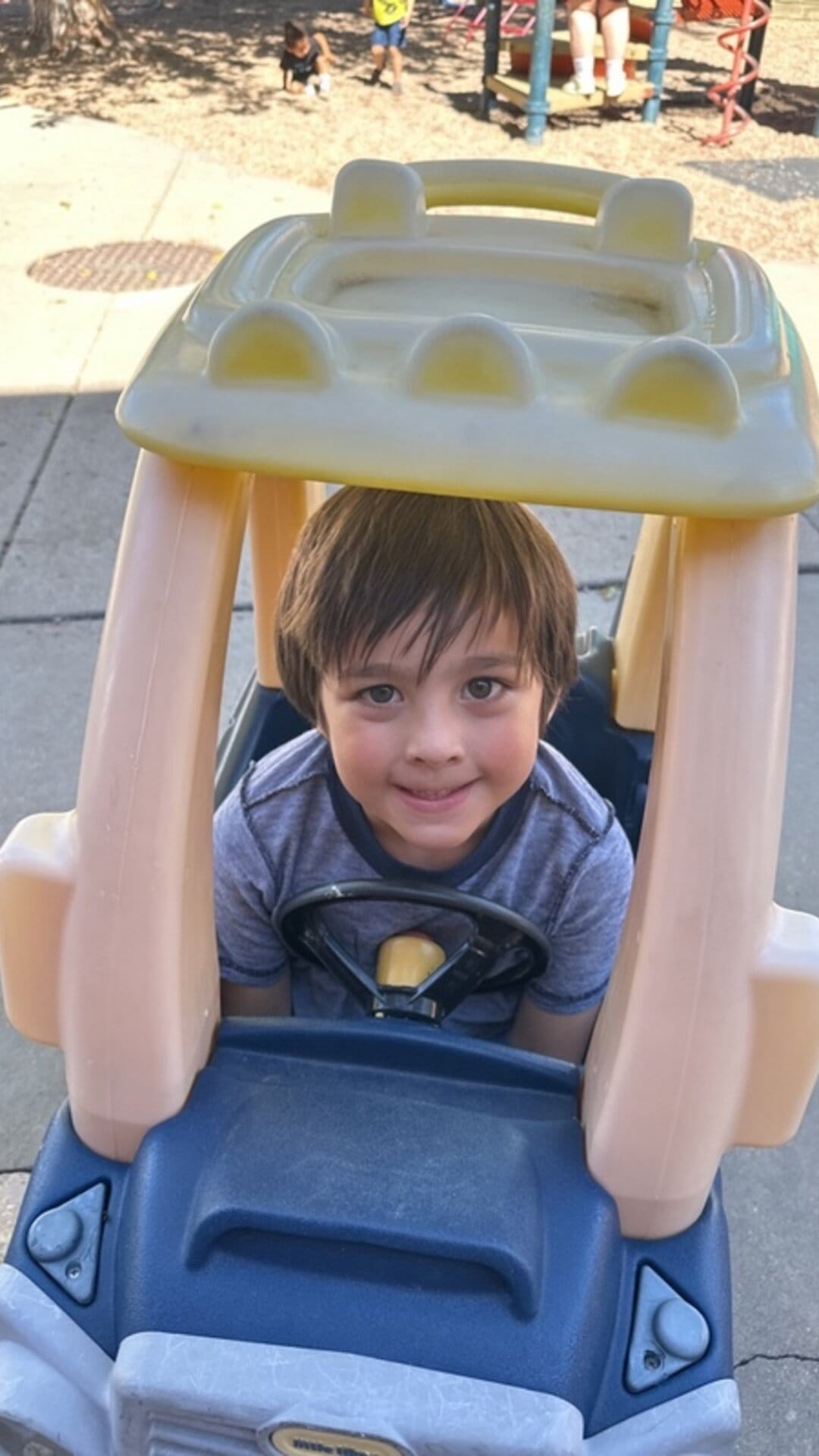 Smiling boy driving a ride-on toy car on the playground