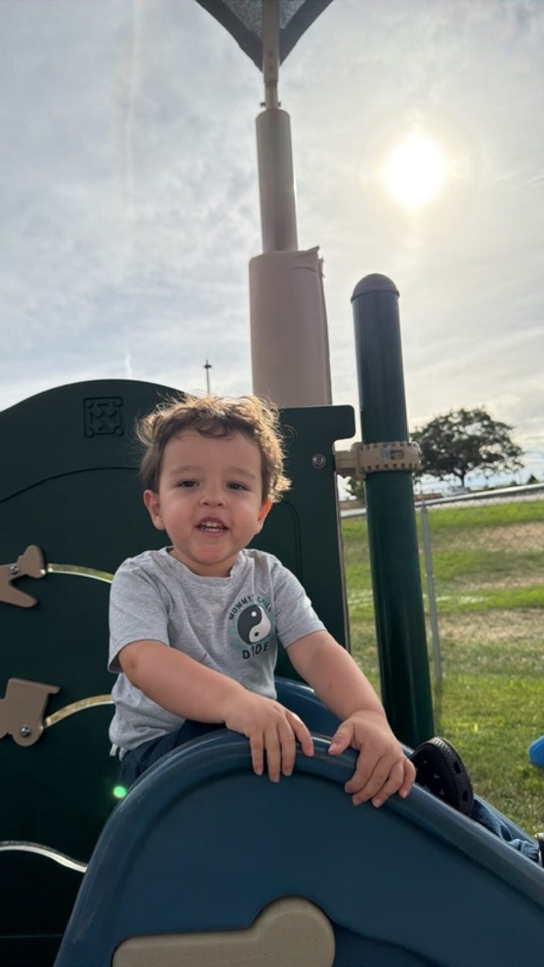 Toddler smiling at the top of a playground slide on a sunny day